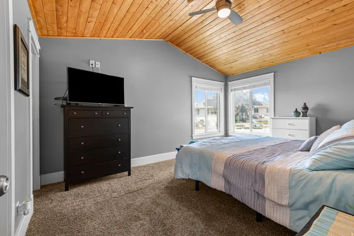 Vaulted wood-paneled ceiling with a flush-mount ceiling fan, gray painted walls, and two large windows with white trim