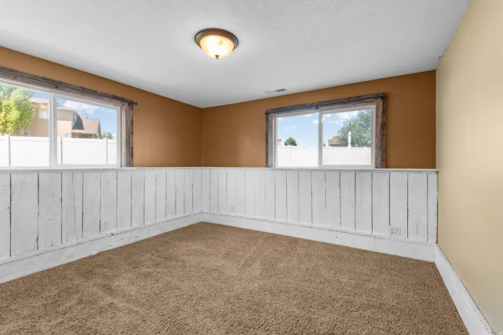 Bright corner room showcasing neutral two-tone walls with white vertical shiplap wainscoting, warm bronze upper walls, and large amount of natural light with above grade windows.
