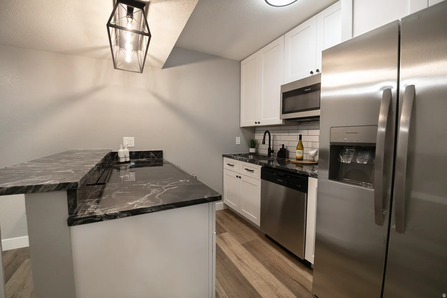 Contemporary kitchen featuring dark patterned countertops, white shaker cabinetry, stainless steel appliances, and wood-finish flooring