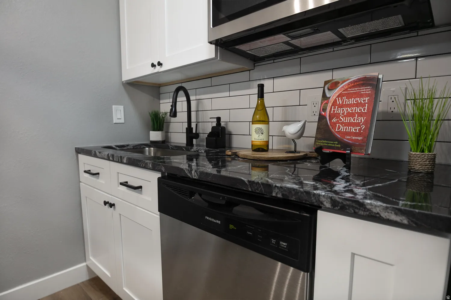 Kitchen area featuring dark patterned countertops, white shaker-style cabinetry, subway tile backsplash, a stainless steel dishwasher, and a black gooseneck faucet