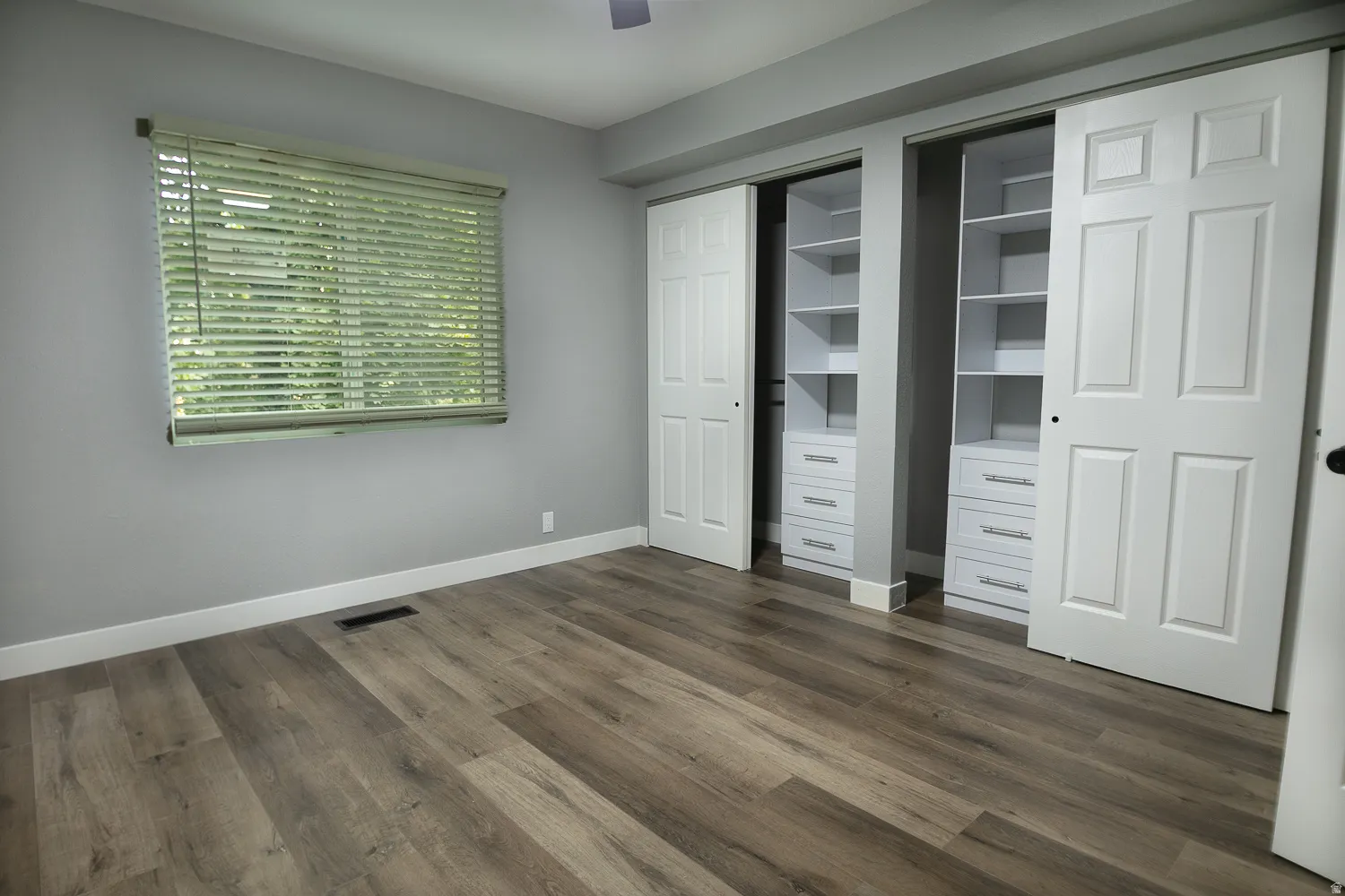 Spacious room featuring wood-finish flooring, light gray wall tones, and white baseboards
