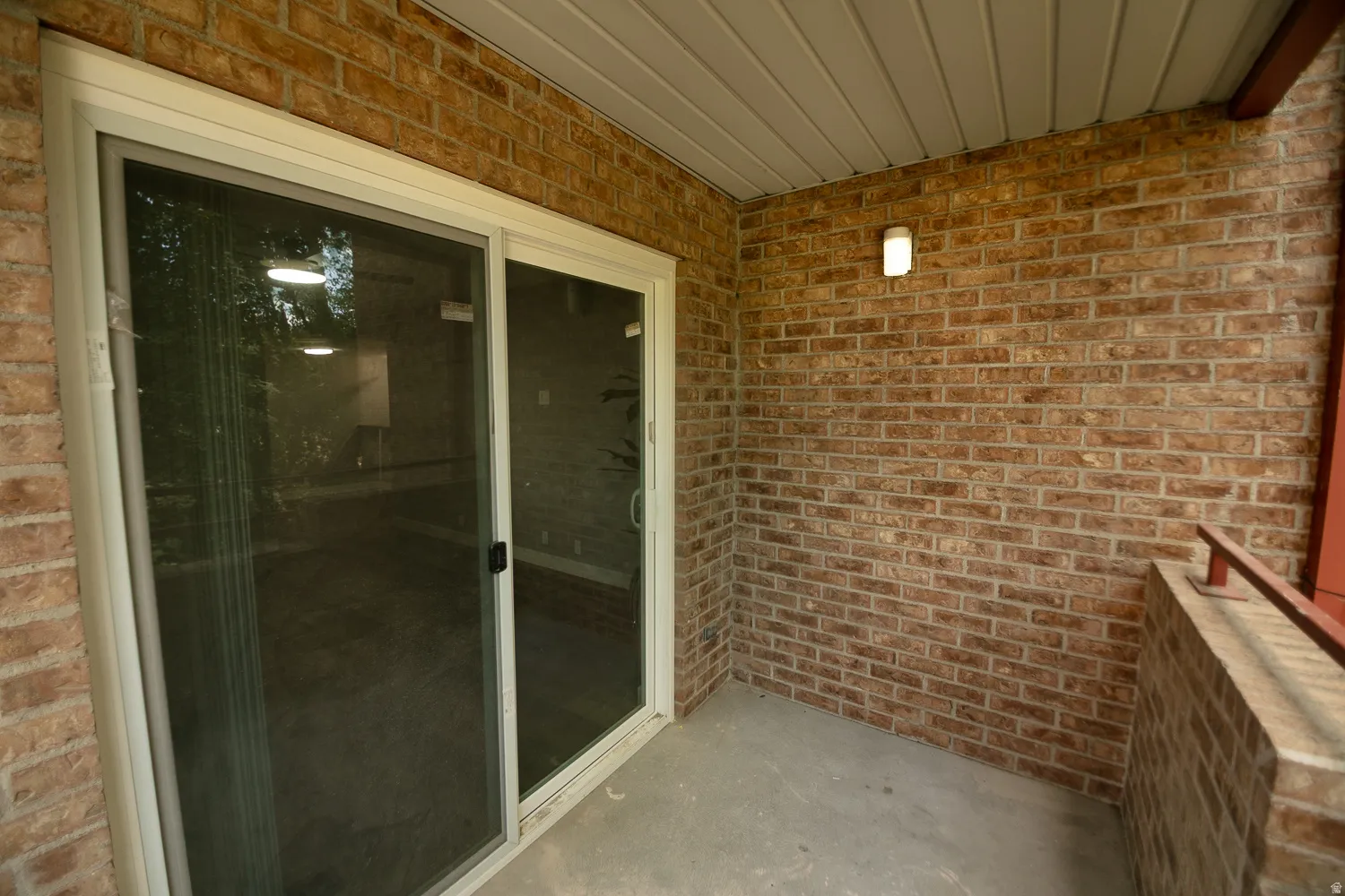 Covered patio featuring a sliding glass door, brick wall construction, concrete flooring, and an exterior wall light fixture