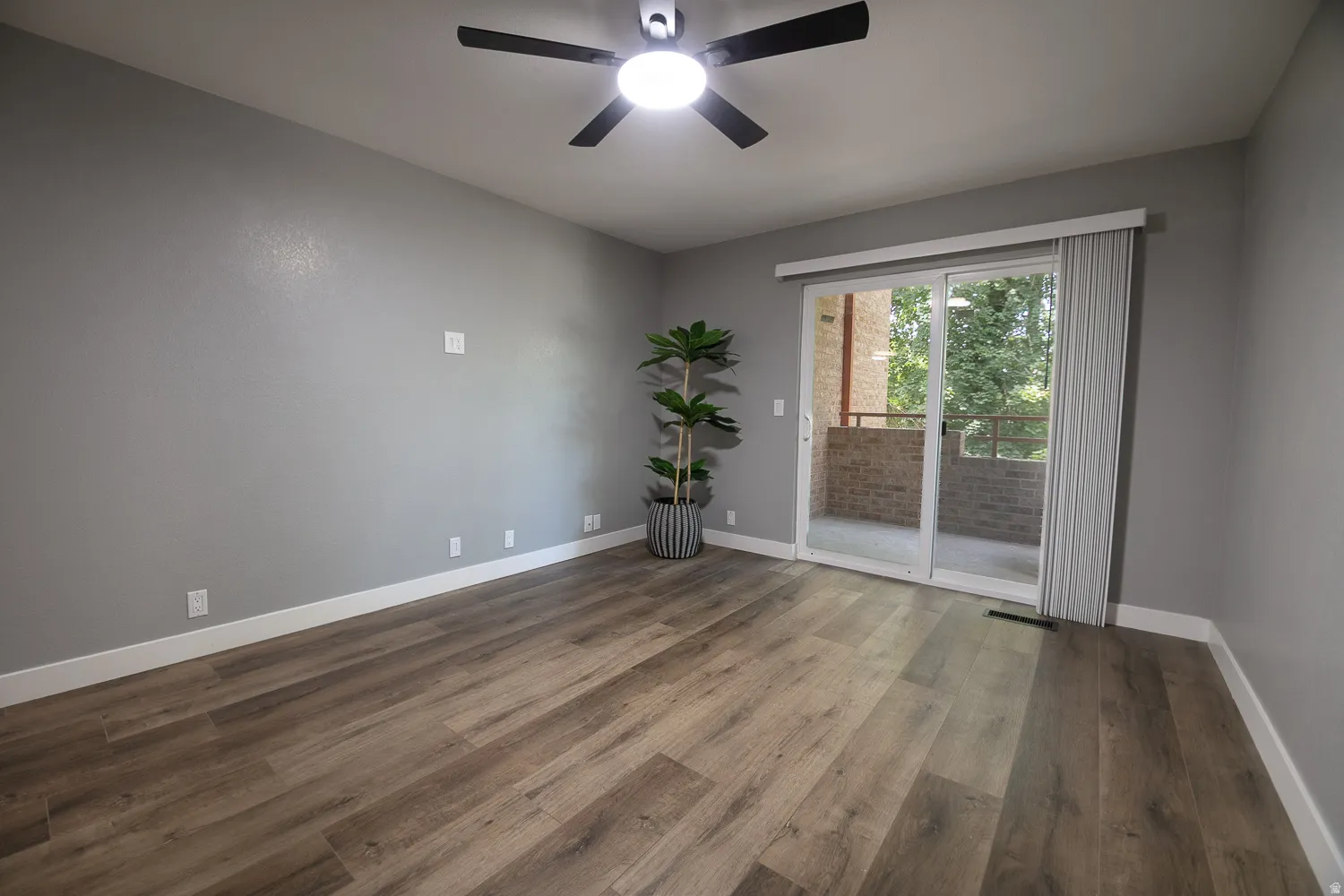 Room featuring wood-finish flooring, light grey walls, and a ceiling fan with integrated lighting