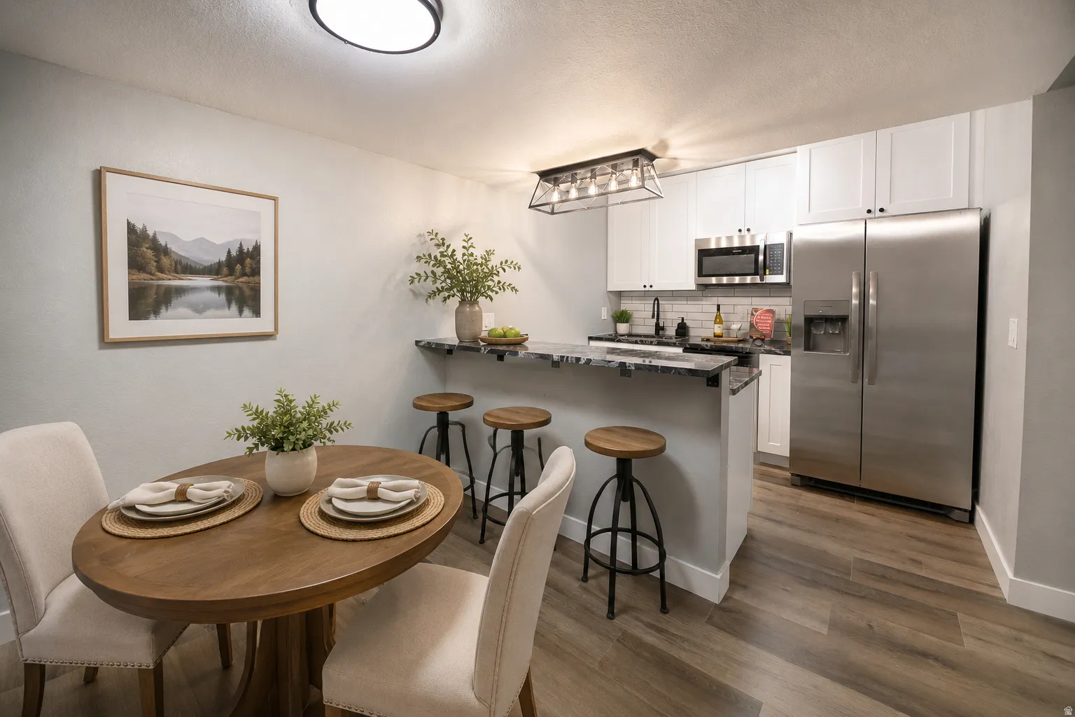 Open-concept kitchen and dining area featuring wood-finish flooring, white cabinetry, stainless steel appliances, a subway tile backsplash, and a breakfast bar with stone-finish countertops