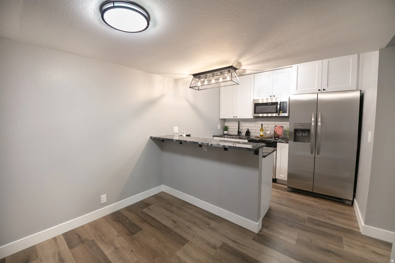 Kitchen with white shaker cabinetry, stainless steel appliances, and a dark granite breakfast bar