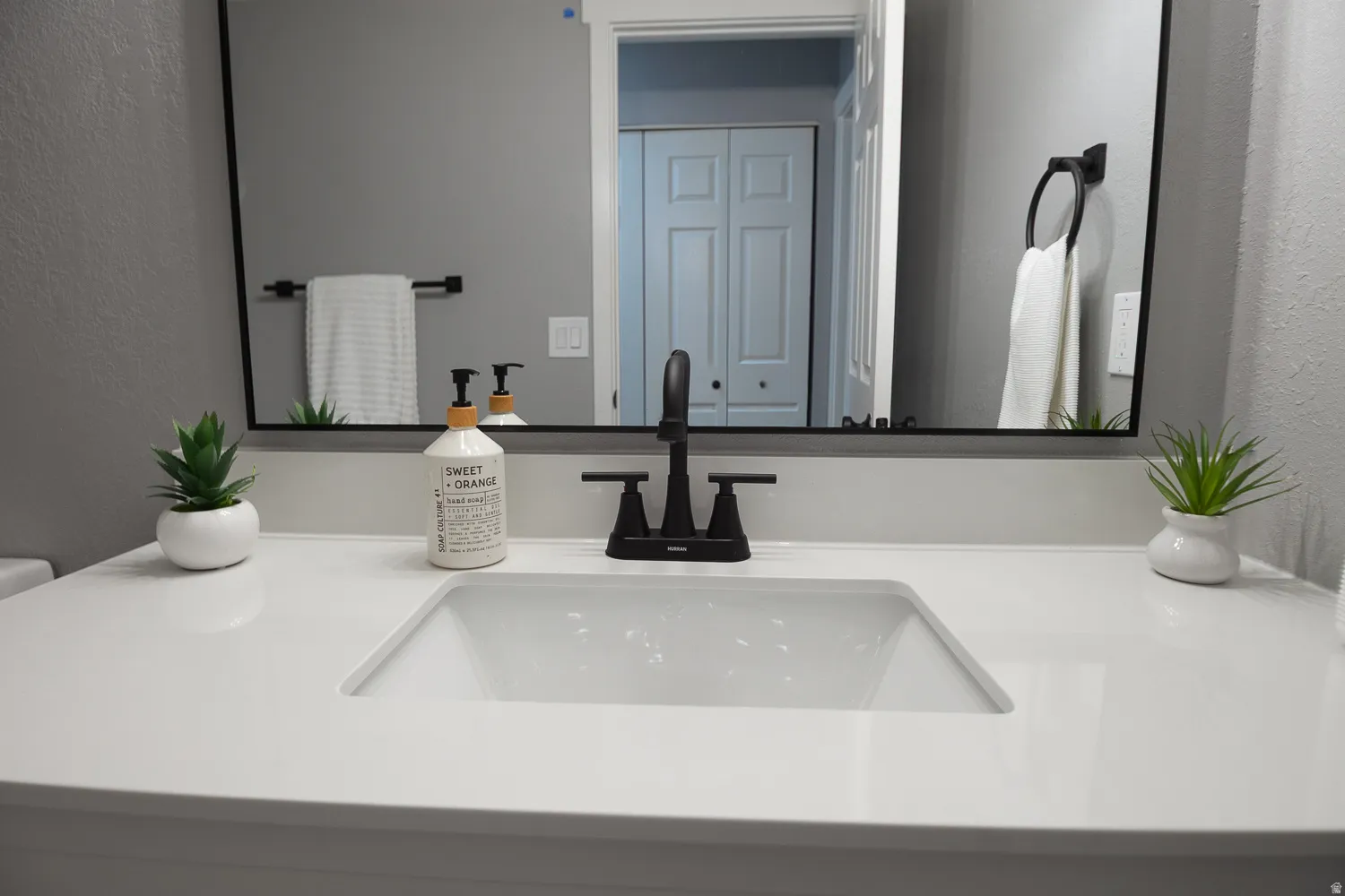 Bathroom vanity featuring a white countertop with an integrated rectangular sink, a black faucet, and a large mirror with a black frame