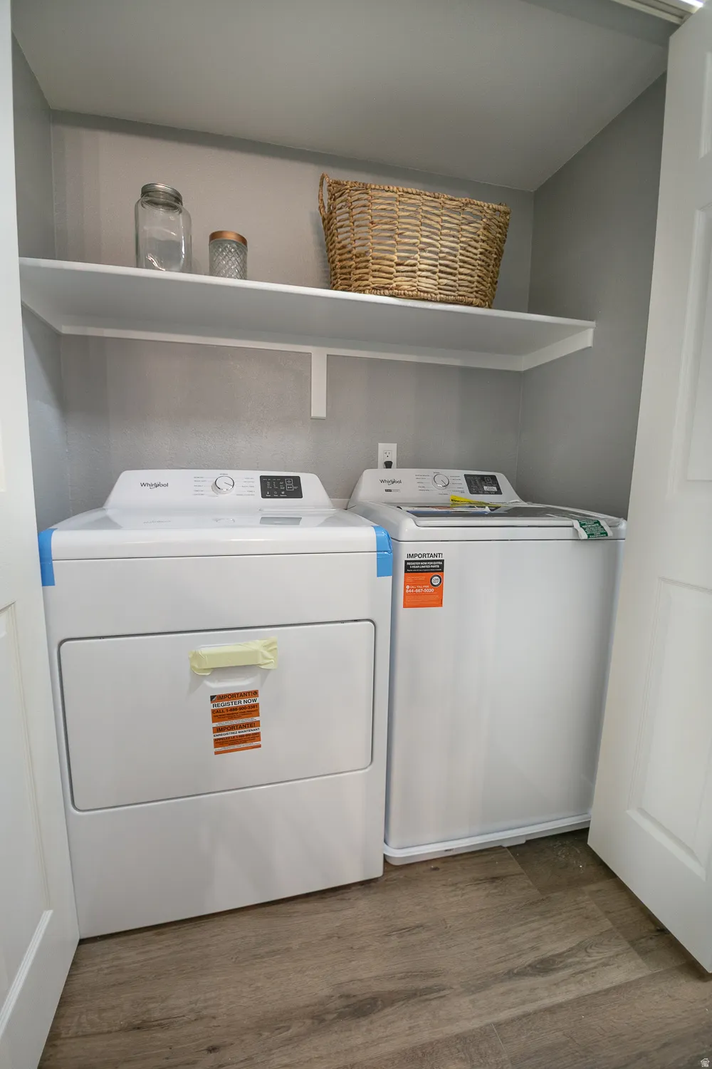 Dedicated laundry area featuring wood-finish flooring, a white floating shelf, and neutral gray wall paint