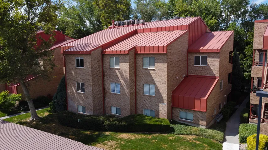 Multi-story brick building featuring a red metal roof and multiple windows with white frames