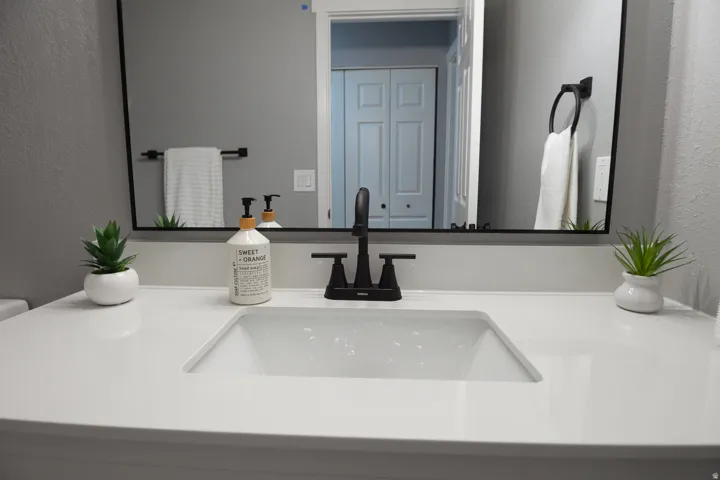 Bathroom vanity featuring a white countertop with an integrated rectangular sink, a black faucet, and a large mirror with a black frame