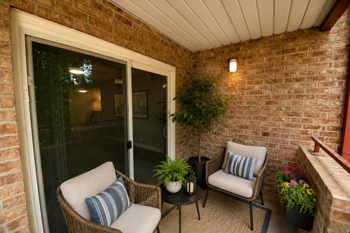 Private patio featuring a brick accent wall, white vinyl sliding glass door, and overhead lighting
