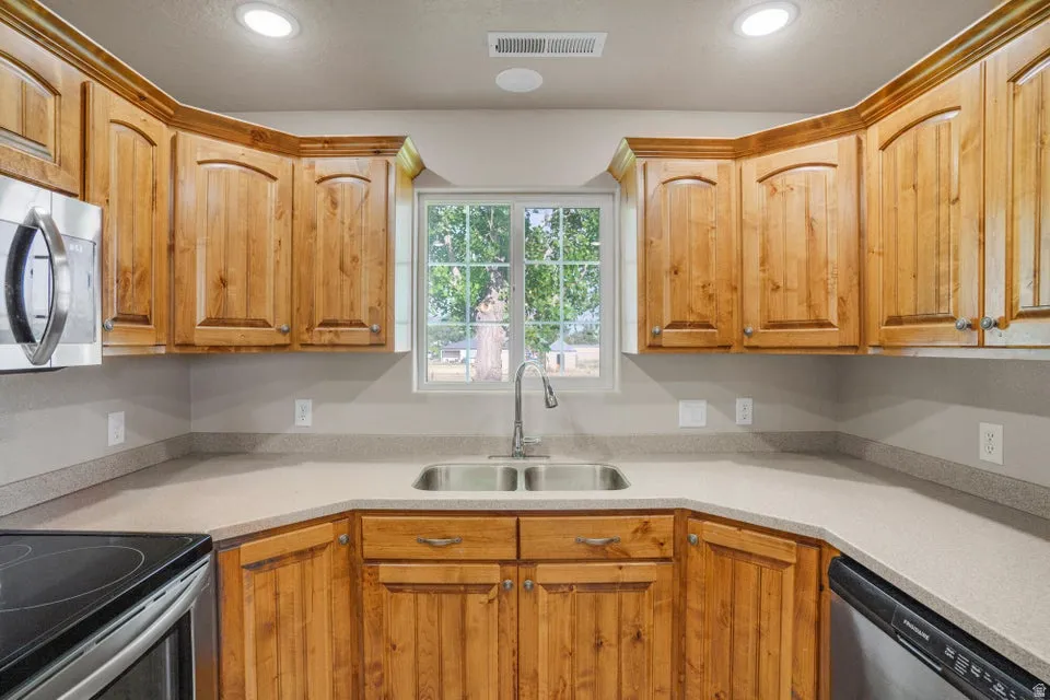 Kitchen featuring wood cabinetry, light-toned countertops, a stainless steel double basin sink, and a window with exterior visibility
