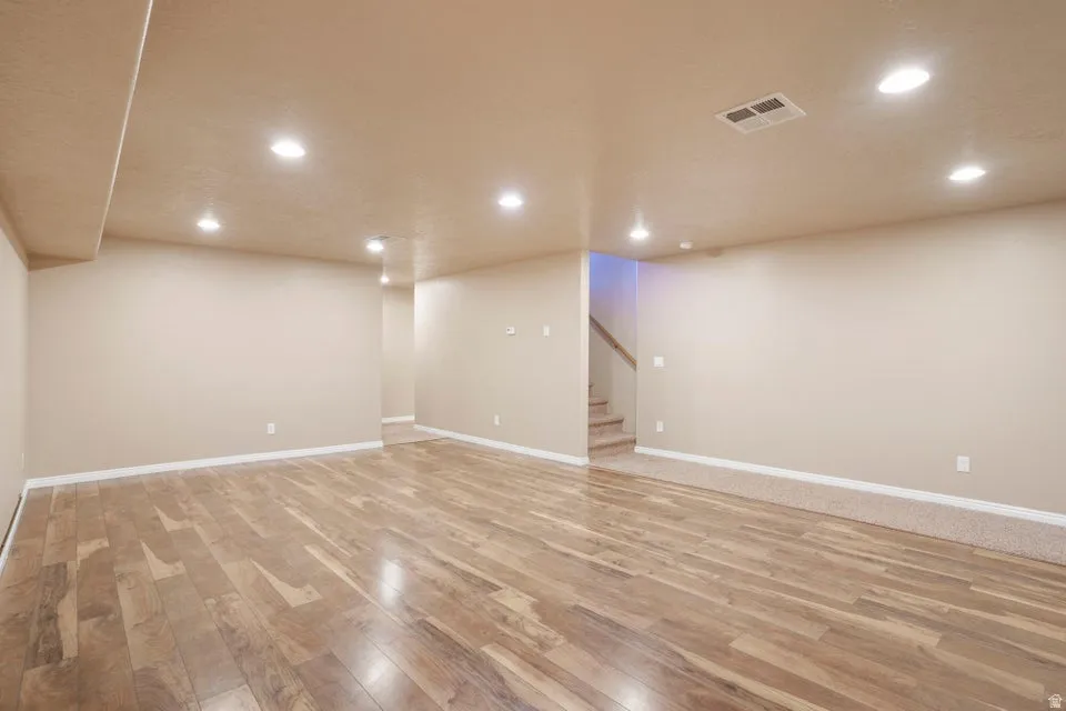 Spacious room featuring wood-finish flooring, recessed lighting, neutral wall tones, white baseboards, and a carpeted section