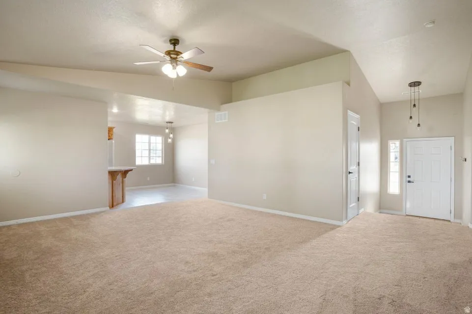 Spacious open-concept living area featuring vaulted ceilings, neutral-toned carpeting, and a ceiling fan with integrated lighting