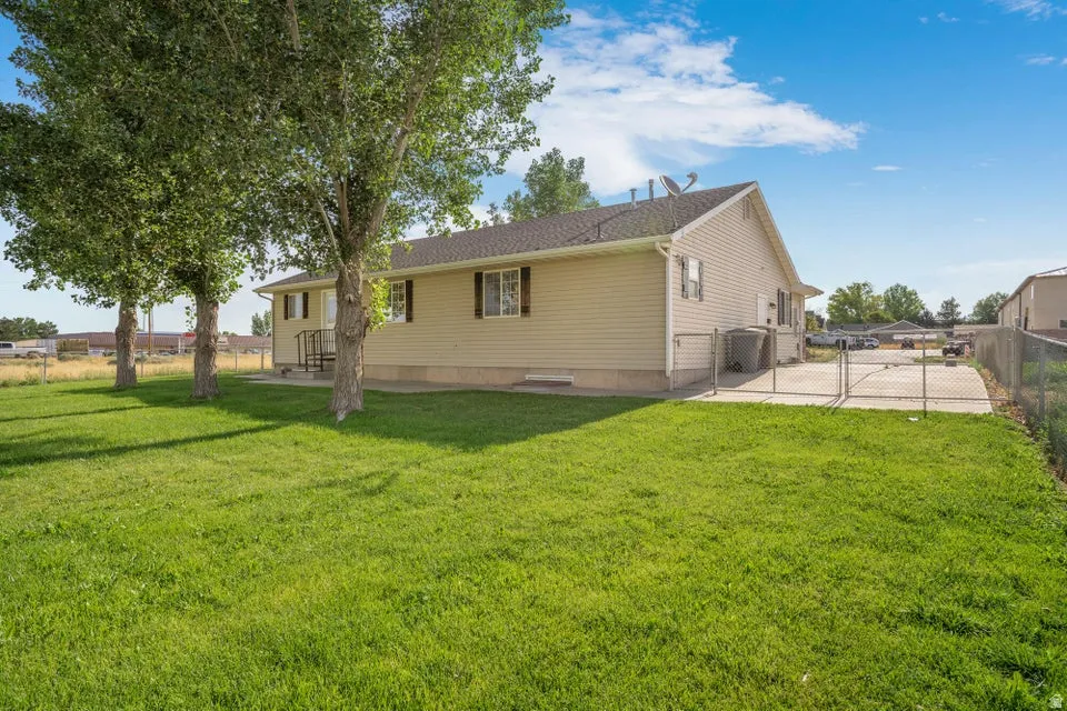 Spacious backyard featuring a substantial lawn area, mature trees, and a concrete patio