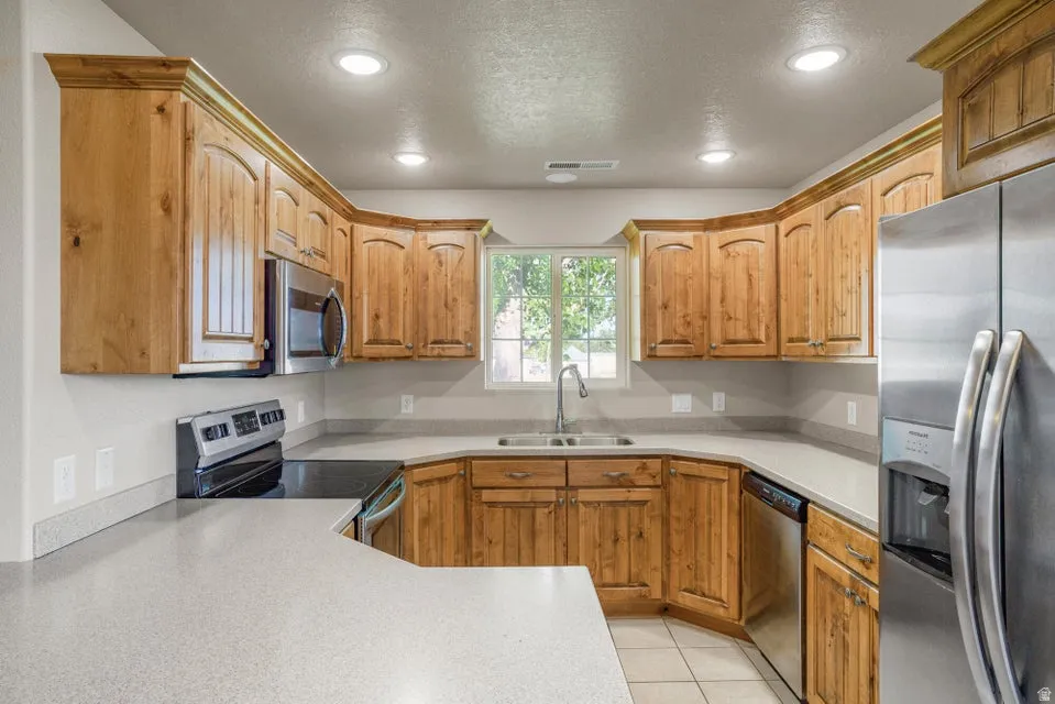 Kitchen featuring wood cabinetry with crown molding, light-toned countertops, a stainless steel sink with a gooseneck faucet, and recessed lighting