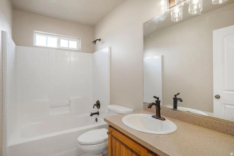 Bathroom featuring a white bathtub and integrated shower, bronze fixtures, a vanity with a laminate countertop, and an oval sink