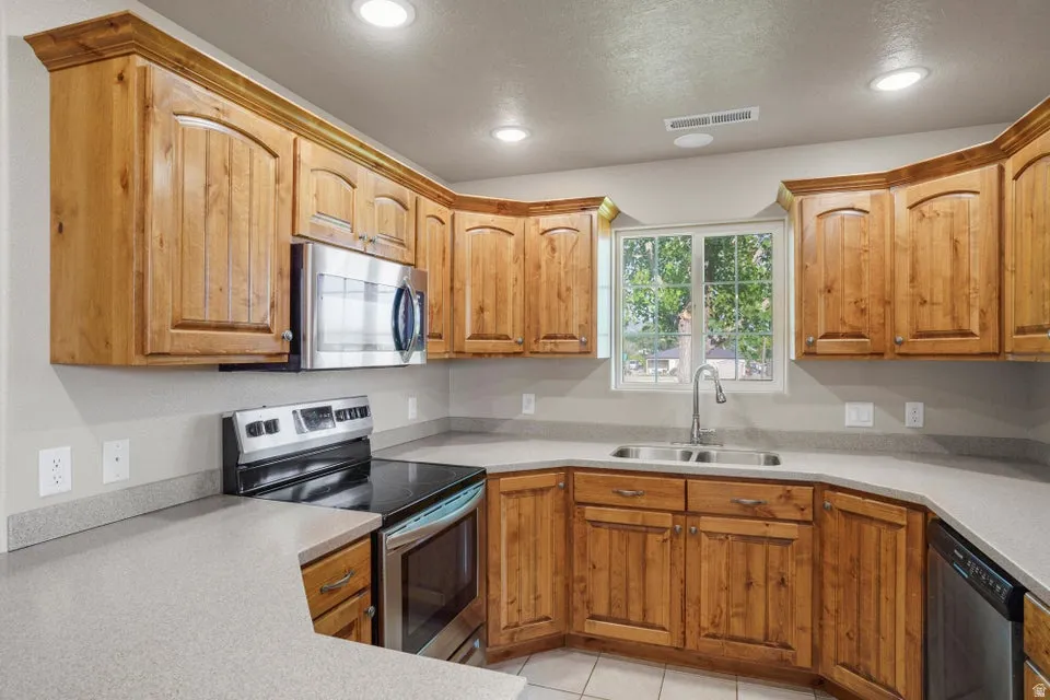 Kitchen featuring wood cabinetry with crown molding, light-toned countertops, stainless steel appliances, and an undermount double basin sink