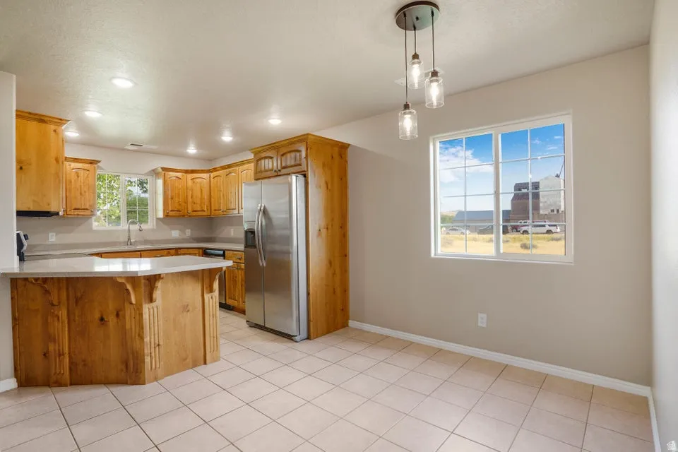 Open-concept kitchen and dining area featuring light wood cabinetry, a stainless steel refrigerator, recessed lighting, and a window with exterior views