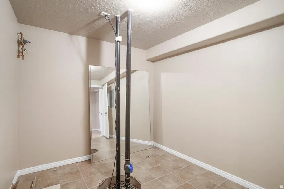 Utility area with neutral wall paint, tiled flooring, white baseboards, and overhead lighting