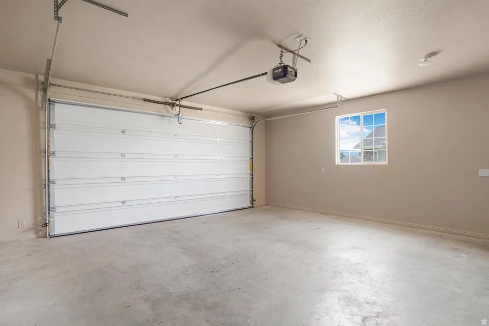 Spacious garage featuring a large white sectional garage door, concrete flooring, automatic garage door opener, and a white-framed window