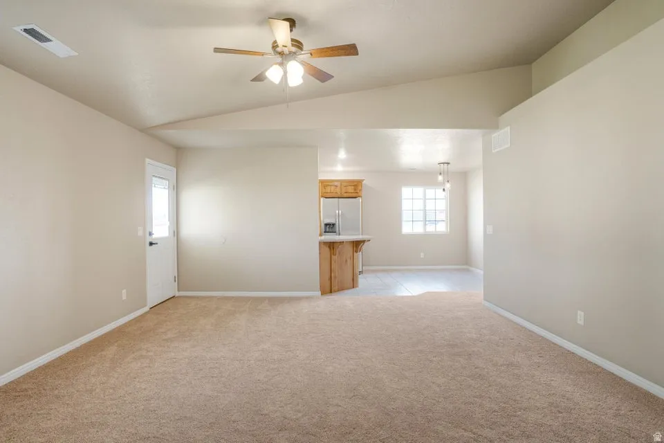 Spacious living area featuring neutral carpeting and vaulted ceilings