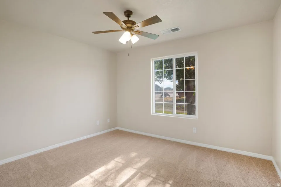 Carpeted room featuring neutral-toned walls, a white-framed window with grid panes, and a ceiling fan with integrated lighting