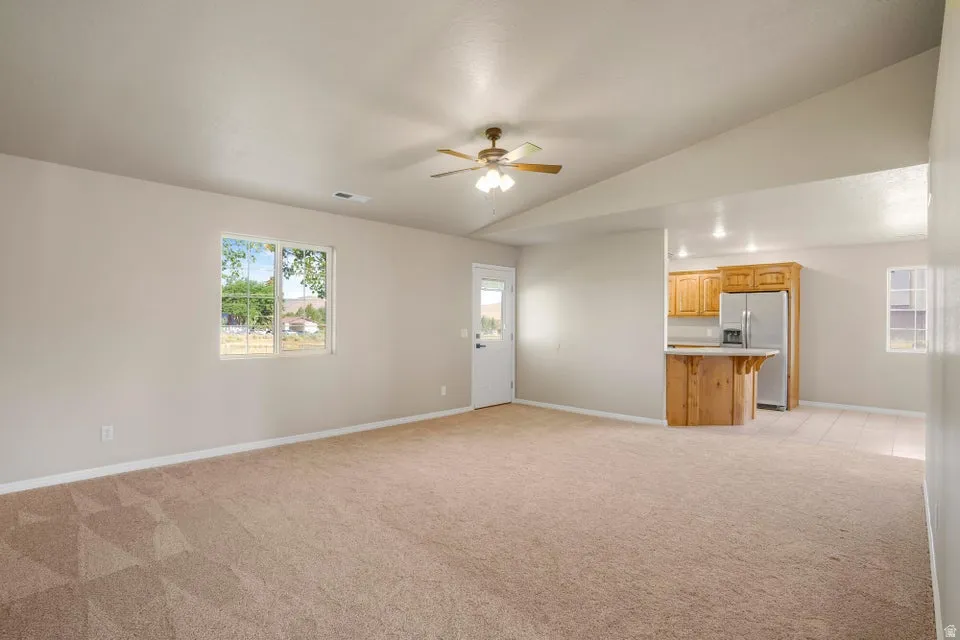 Vaulted ceilings accent this open living space featuring light-toned carpeting, a window providing natural light, and a ceiling fan