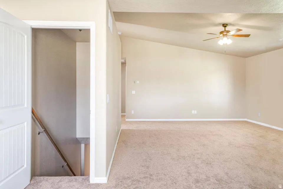 Spacious room featuring vaulted ceilings, neutral-toned walls, and plush carpet flooring