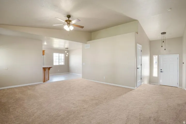 Spacious open-concept living area featuring vaulted ceilings, neutral-toned carpeting, and a ceiling fan with integrated lighting