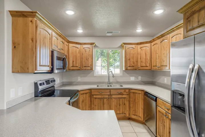 Kitchen featuring wood cabinetry with crown molding, light-toned countertops, a stainless steel sink with a gooseneck faucet, and recessed lighting