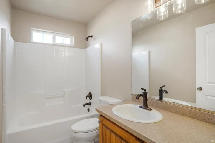 Bathroom featuring a white bathtub and integrated shower, bronze fixtures, a vanity with a laminate countertop, and an oval sink