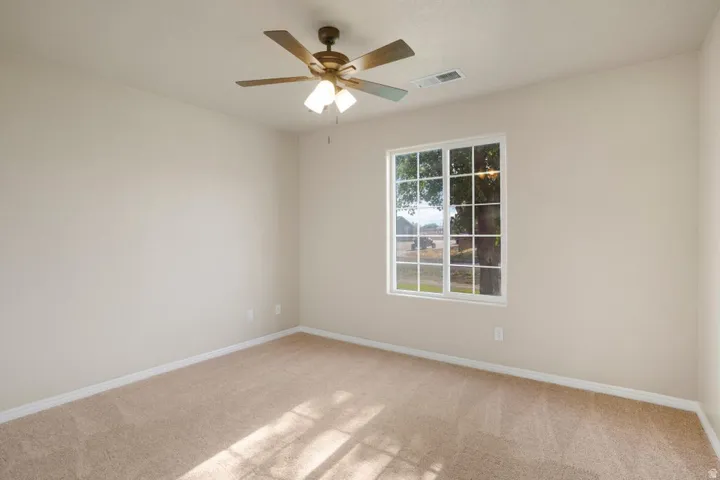Carpeted room featuring neutral-toned walls, a white-framed window with grid panes, and a ceiling fan with integrated lighting