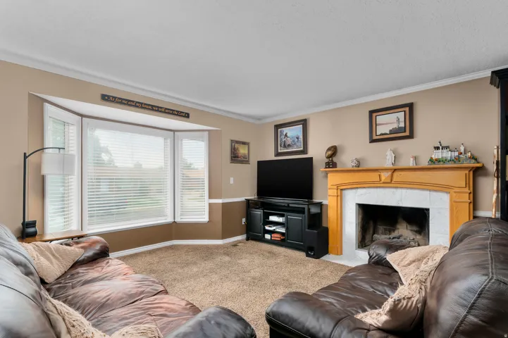 Living area featuring a bay window, natural wood mantel, white tile fireplace surround, and crown molding