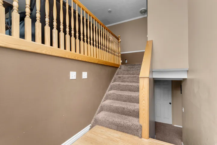 Carpeted staircase with light wood-finish balusters and handrails, complemented by neutral wall tones