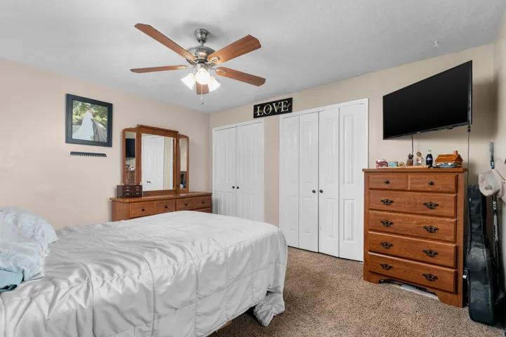 Bedroom featuring plush carpet flooring, a ceiling fan with light fixture, and two sets of bi-fold closet doors