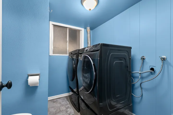 Dedicated laundry area featuring a white-framed window, light blue vertical plank paneling, and an overhead flush-mount light fixture