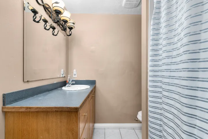 Bathroom featuring a wood-finish vanity with a built-in sink, a wall-mounted mirror, and a multi-bulb light fixture
