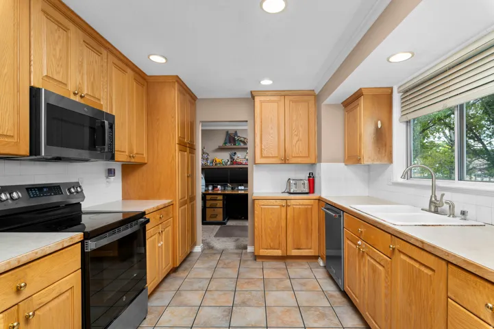 Kitchen featuring light wood cabinetry, stone-finish countertops, stainless steel appliances, tile flooring, and recessed lighting