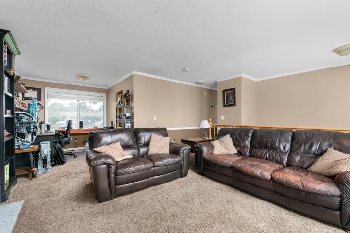 Carpeted loft area featuring a large window, neutral wall paint, white crown molding, and a light wood railing