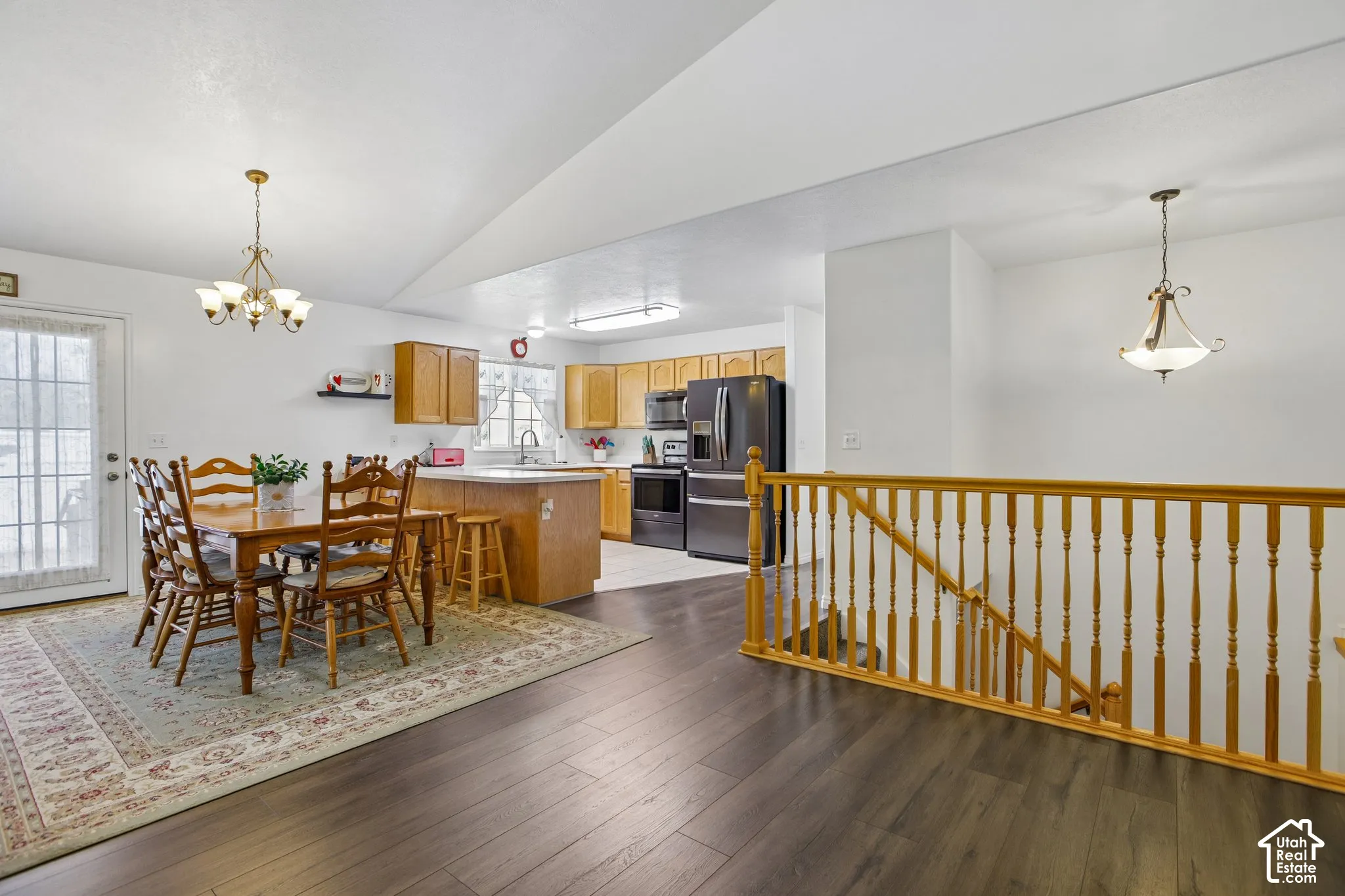 Open-concept living space featuring wood-finish flooring, a wood banister, and a kitchen with light wood cabinetry and dark appliances