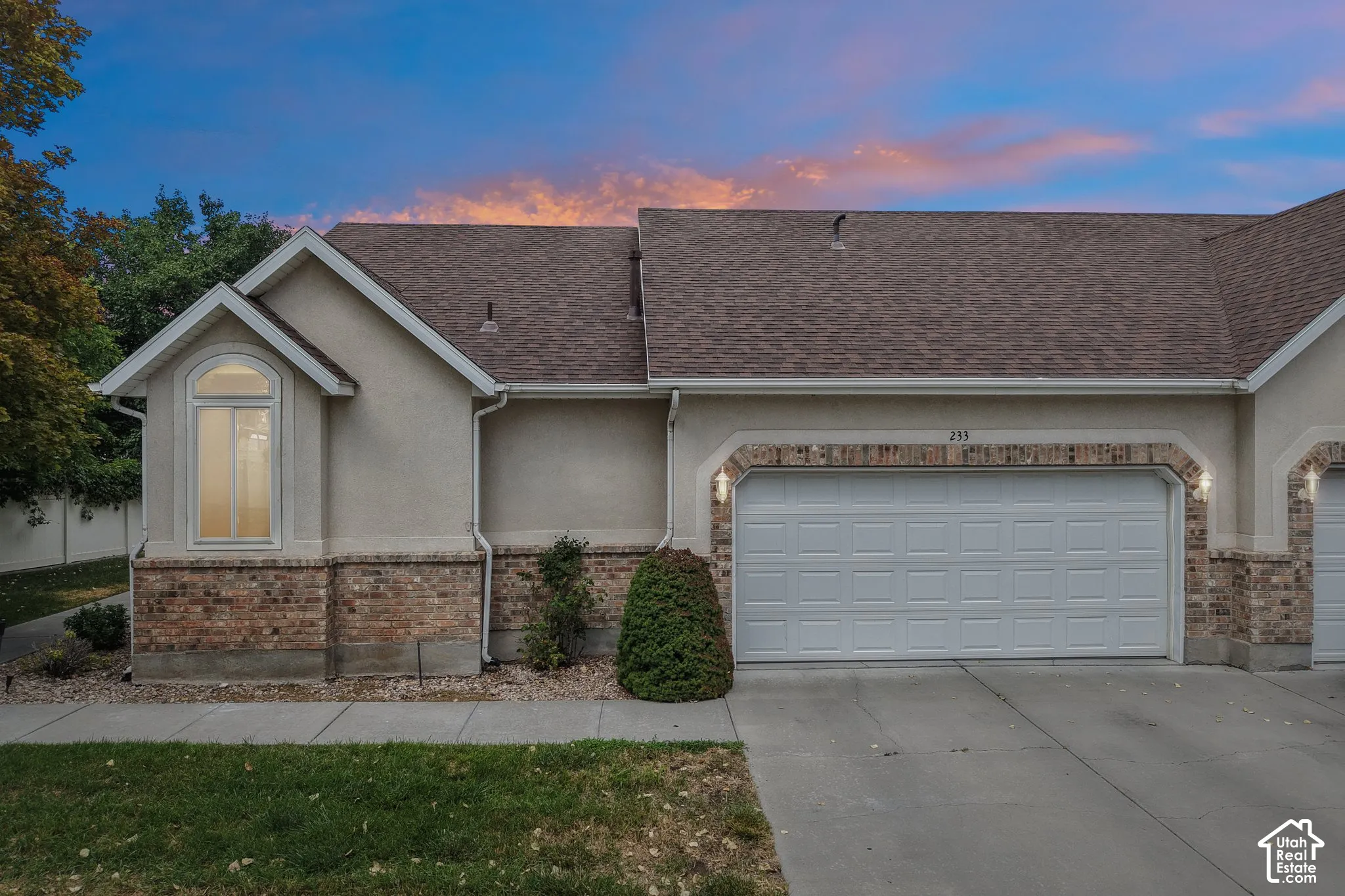 Exterior featuring a two-car garage, brick accents, stucco siding, and an arched window