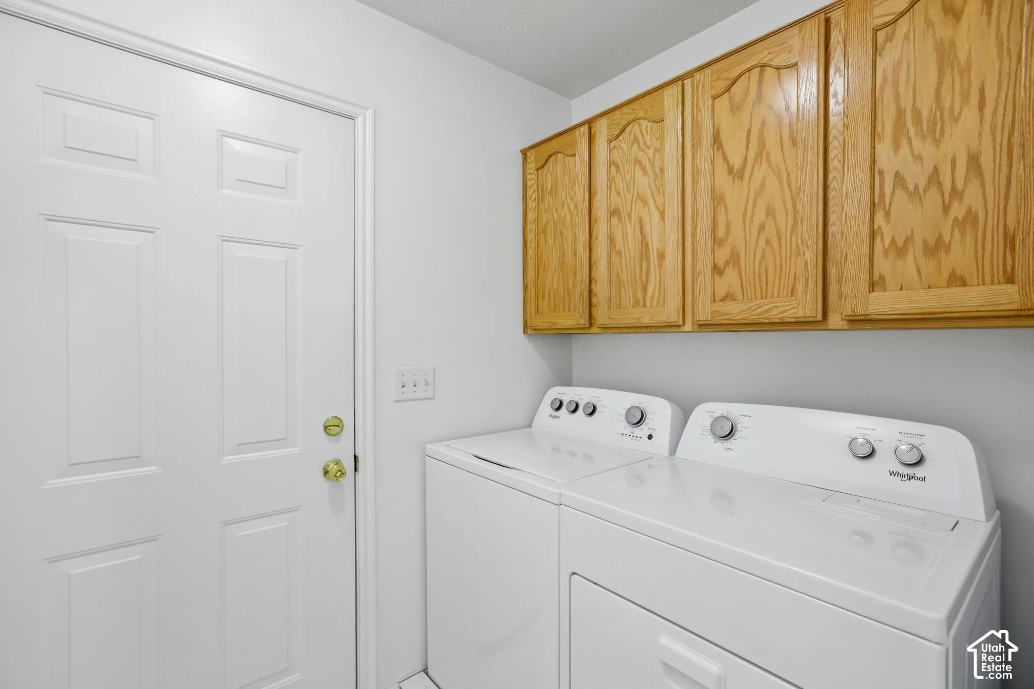 Laundry area featuring a paneled white door, overhead wood cabinetry, and light-colored walls