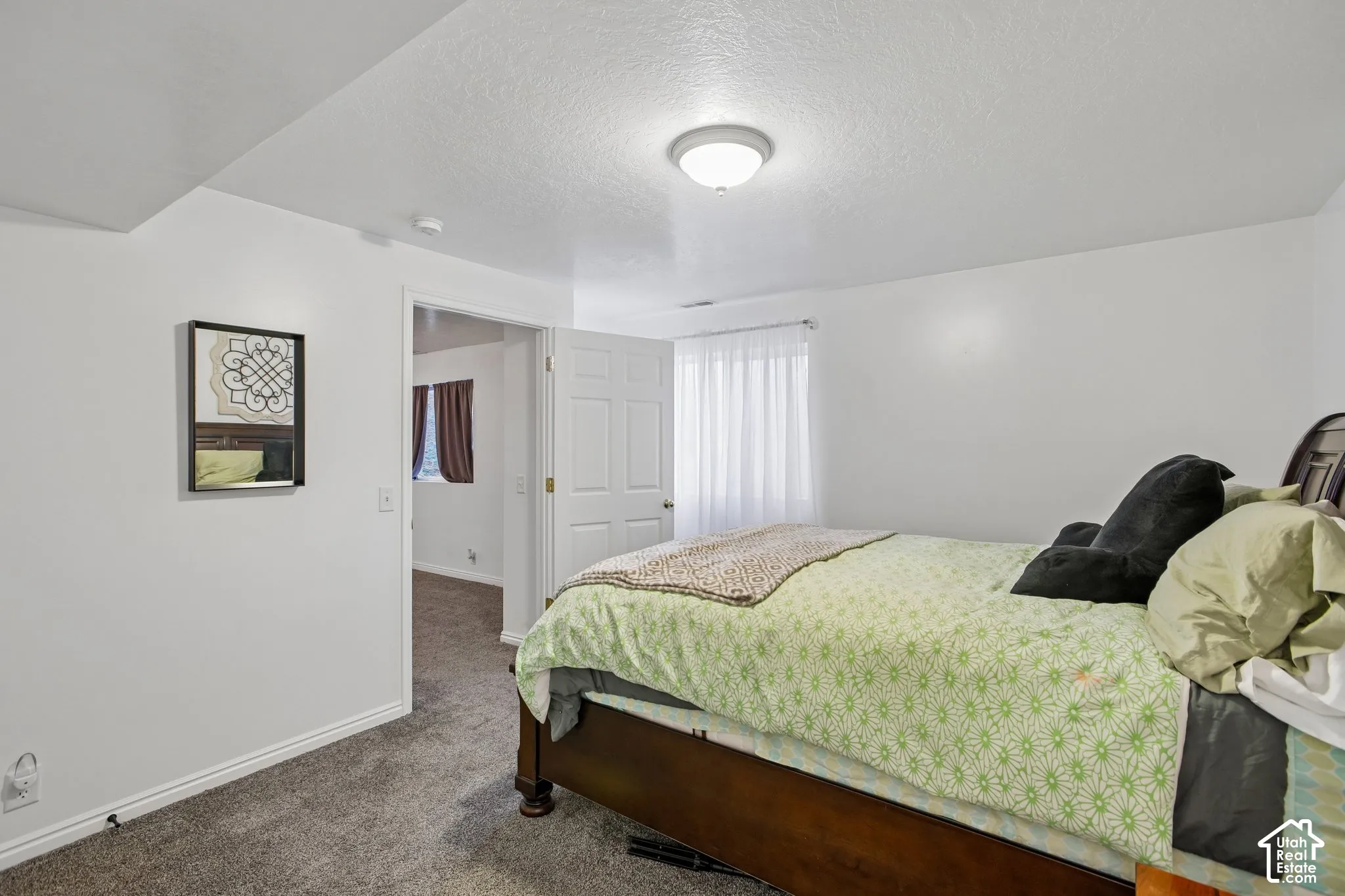 Carpeted room with white walls, a flush-mount ceiling light fixture, and a window with white sheer curtains