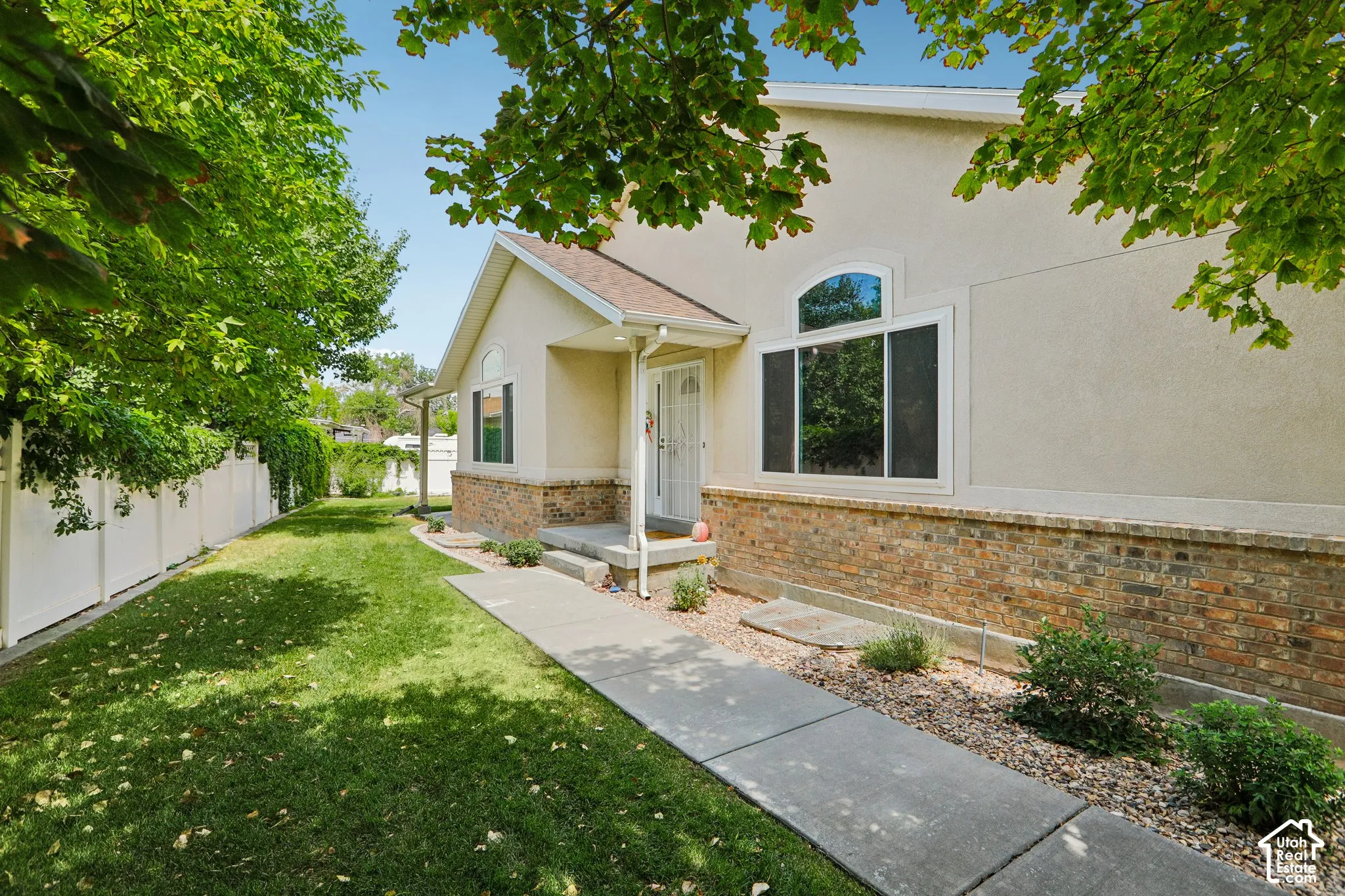 Stucco and brick exterior featuring a covered entry, arched window, and concrete walkway
