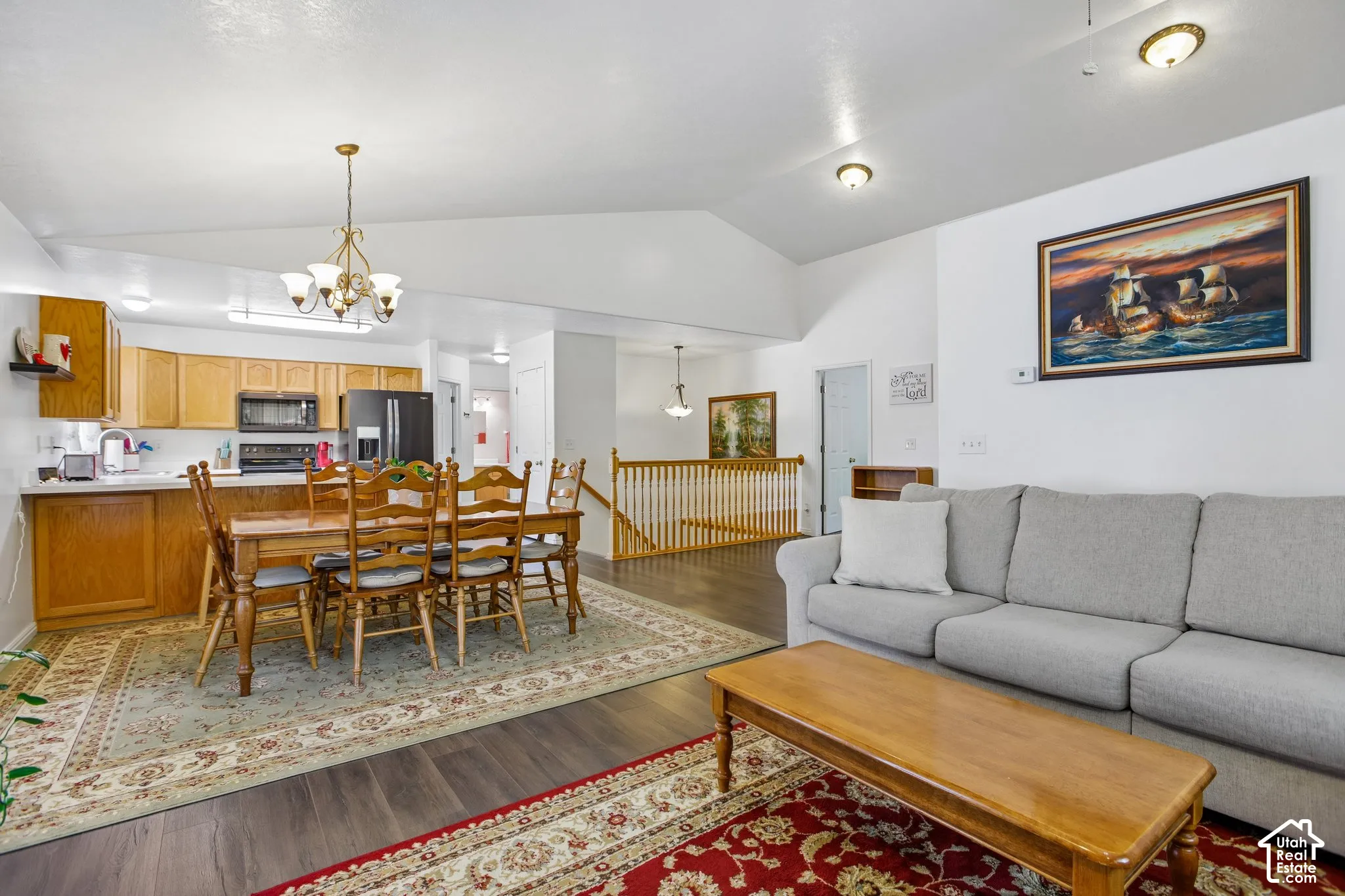Expansive open-concept living area featuring high vaulted ceilings, wood-finish flooring, and a kitchen with light wood cabinetry and dark appliances