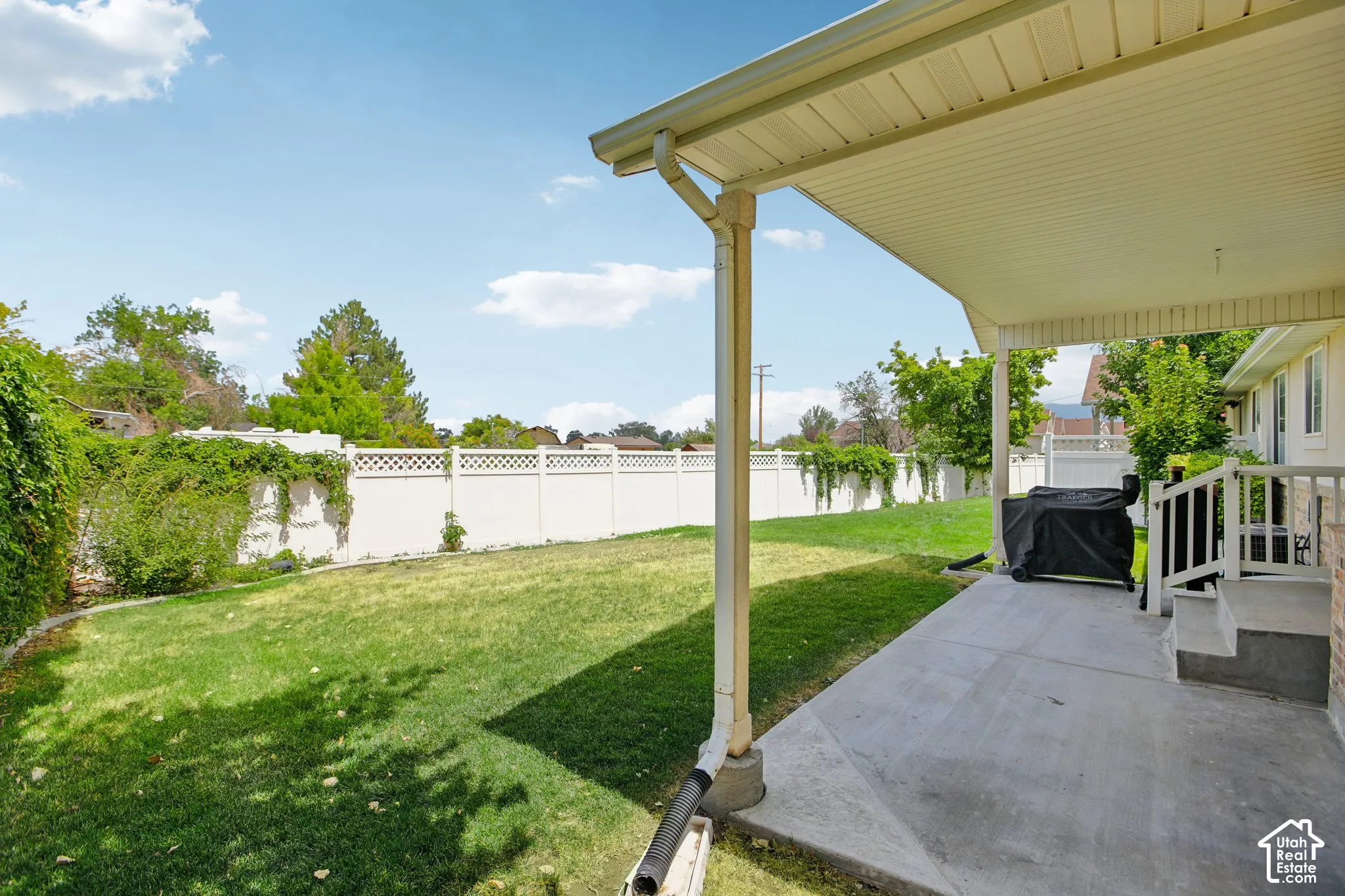 Expansive rear yard featuring a covered patio, concrete surface, and white vinyl fencing