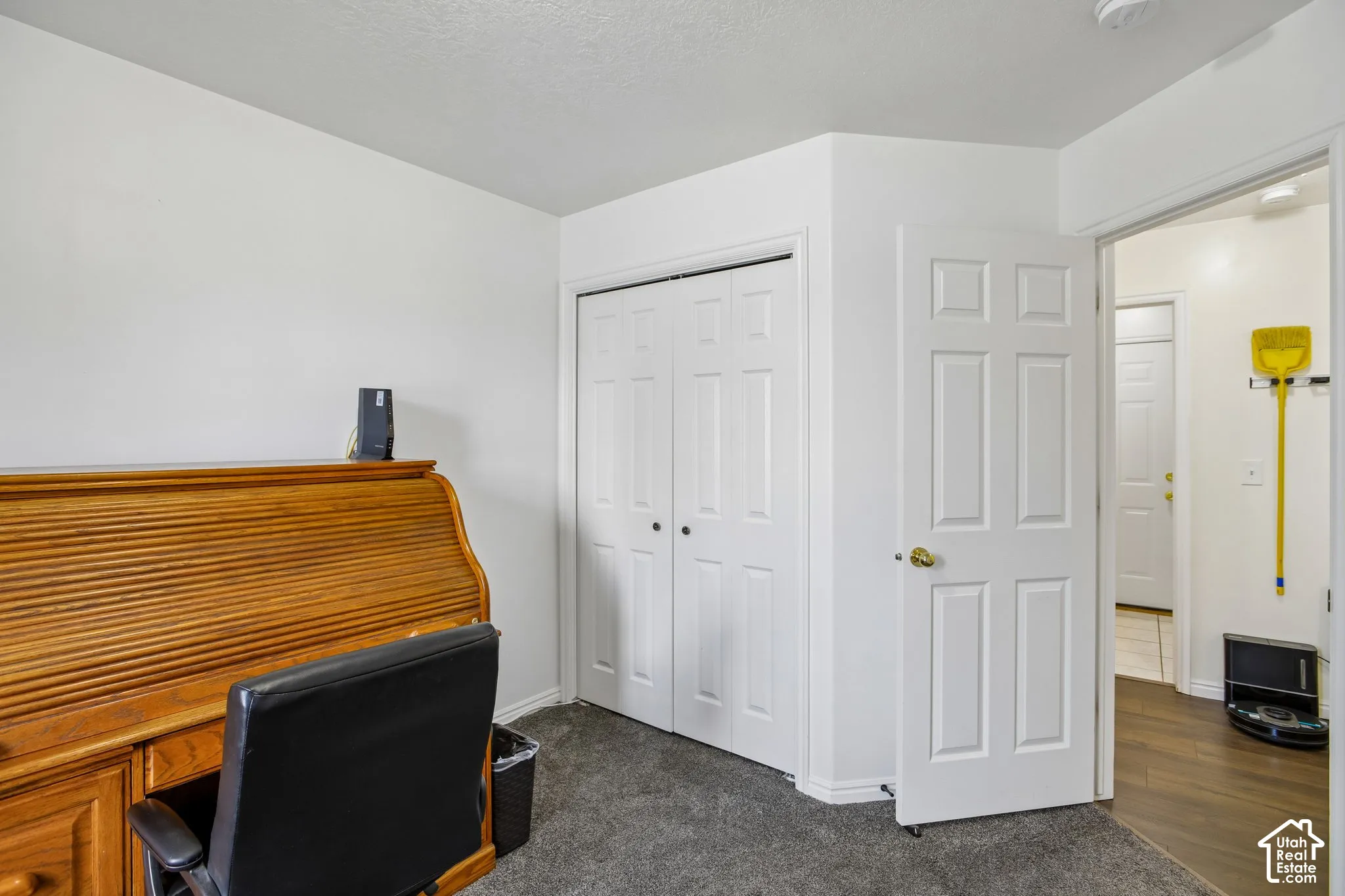 Interior room with neutral wall paint, gray carpeting, a bi-fold closet door, and a paneled door leading to an adjacent space with wood-finish flooring
