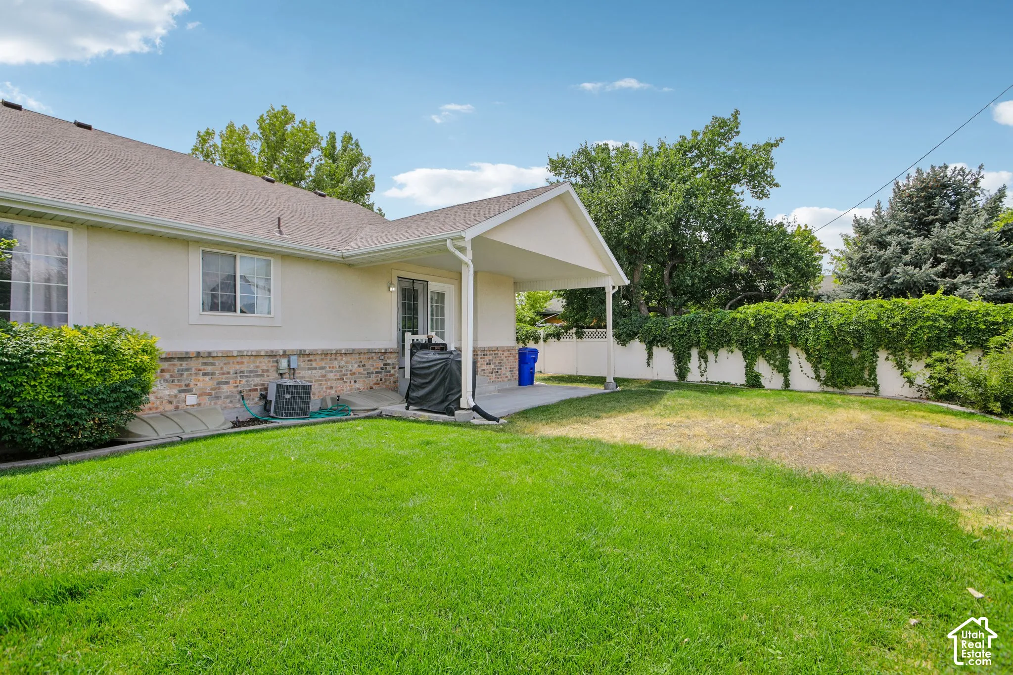 Expansive backyard featuring a manicured lawn, a covered patio, and a white privacy fence with mature vine coverage