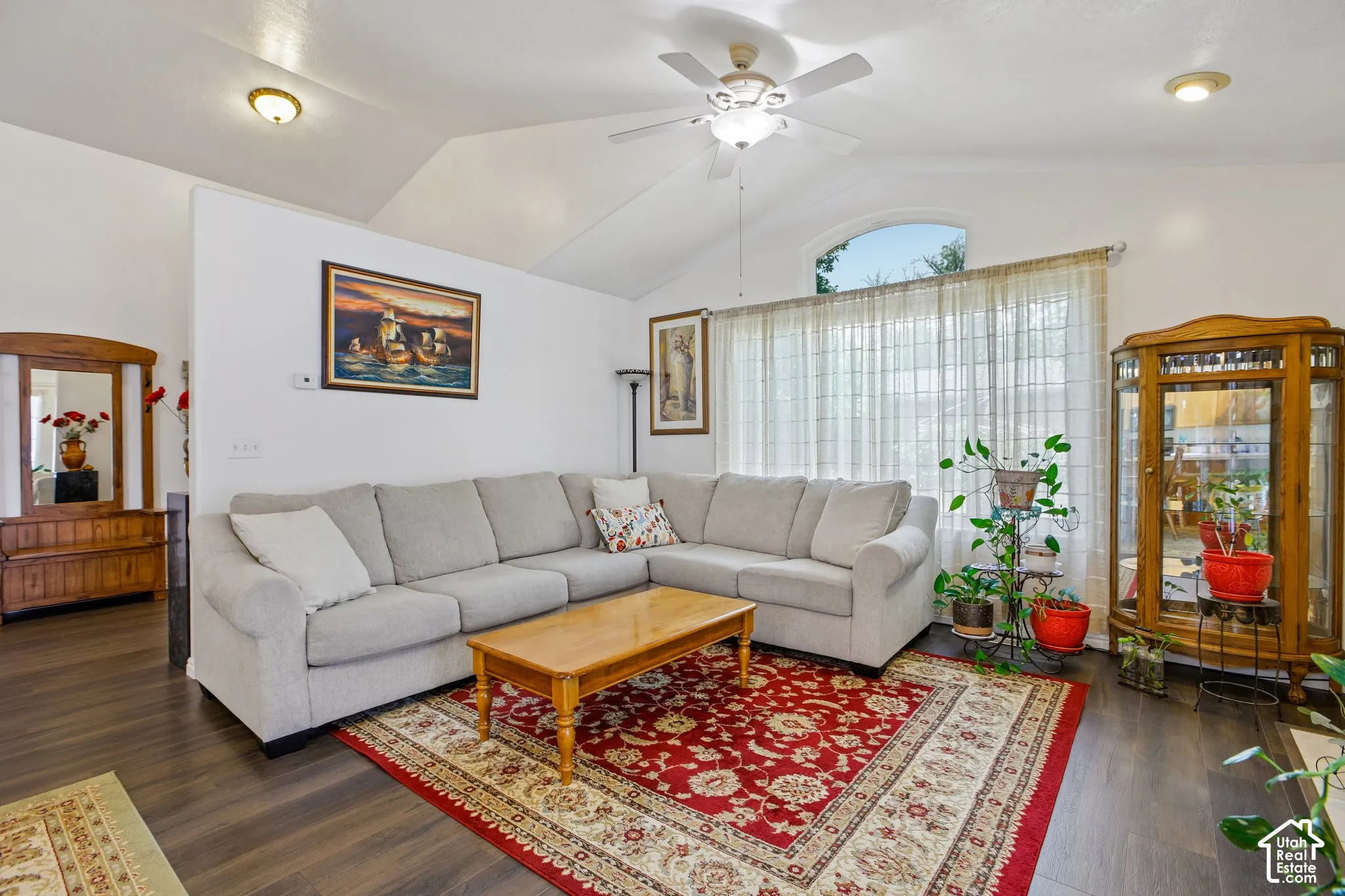 Living area featuring vaulted ceilings, wood-finish flooring, a ceiling fan, and large windows with an arched transom