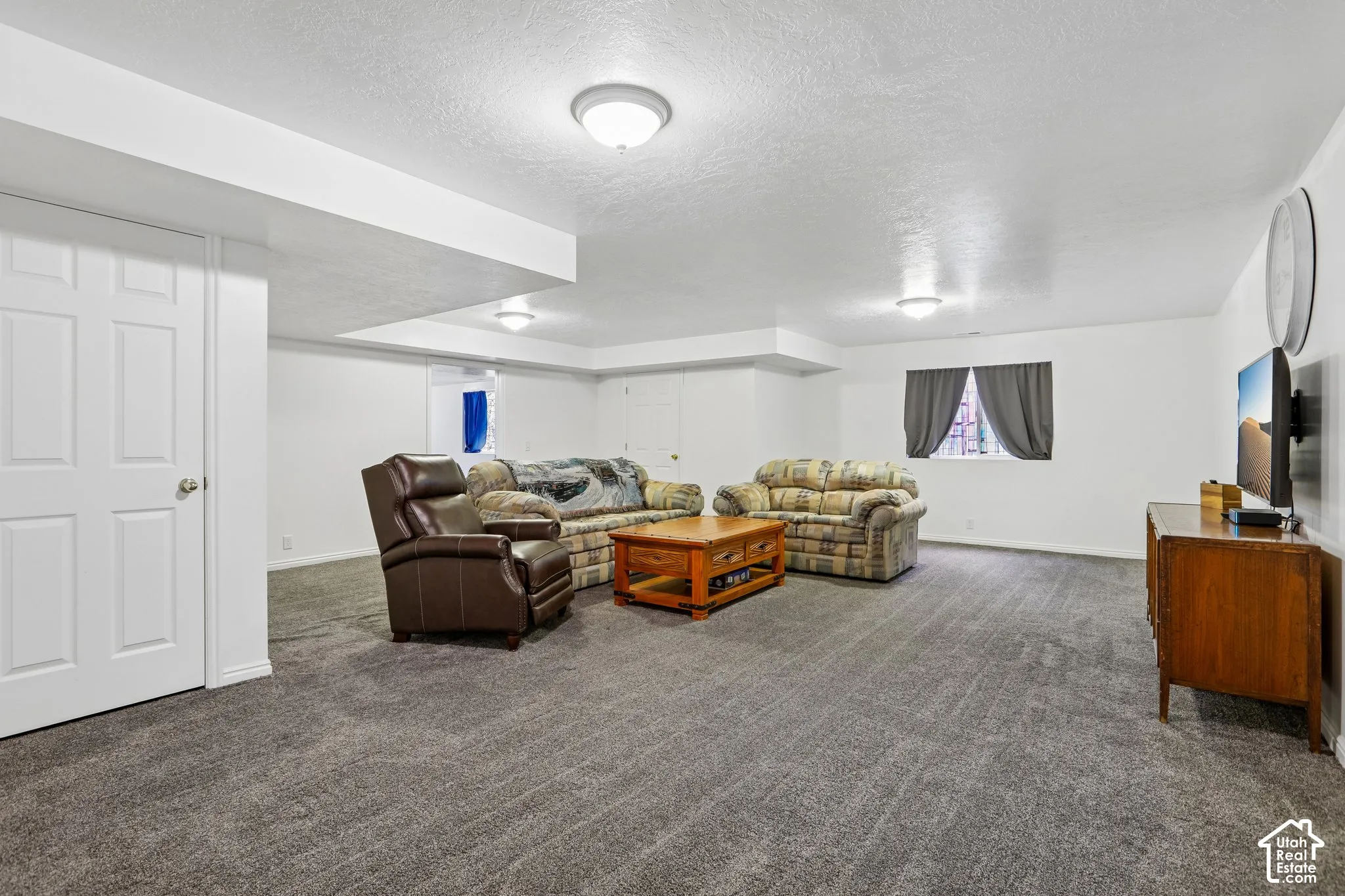 Open living area featuring plush gray carpeting, white painted walls, and ceiling-mounted lighting